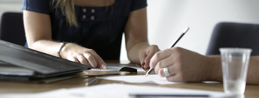 People writing on paper on table.